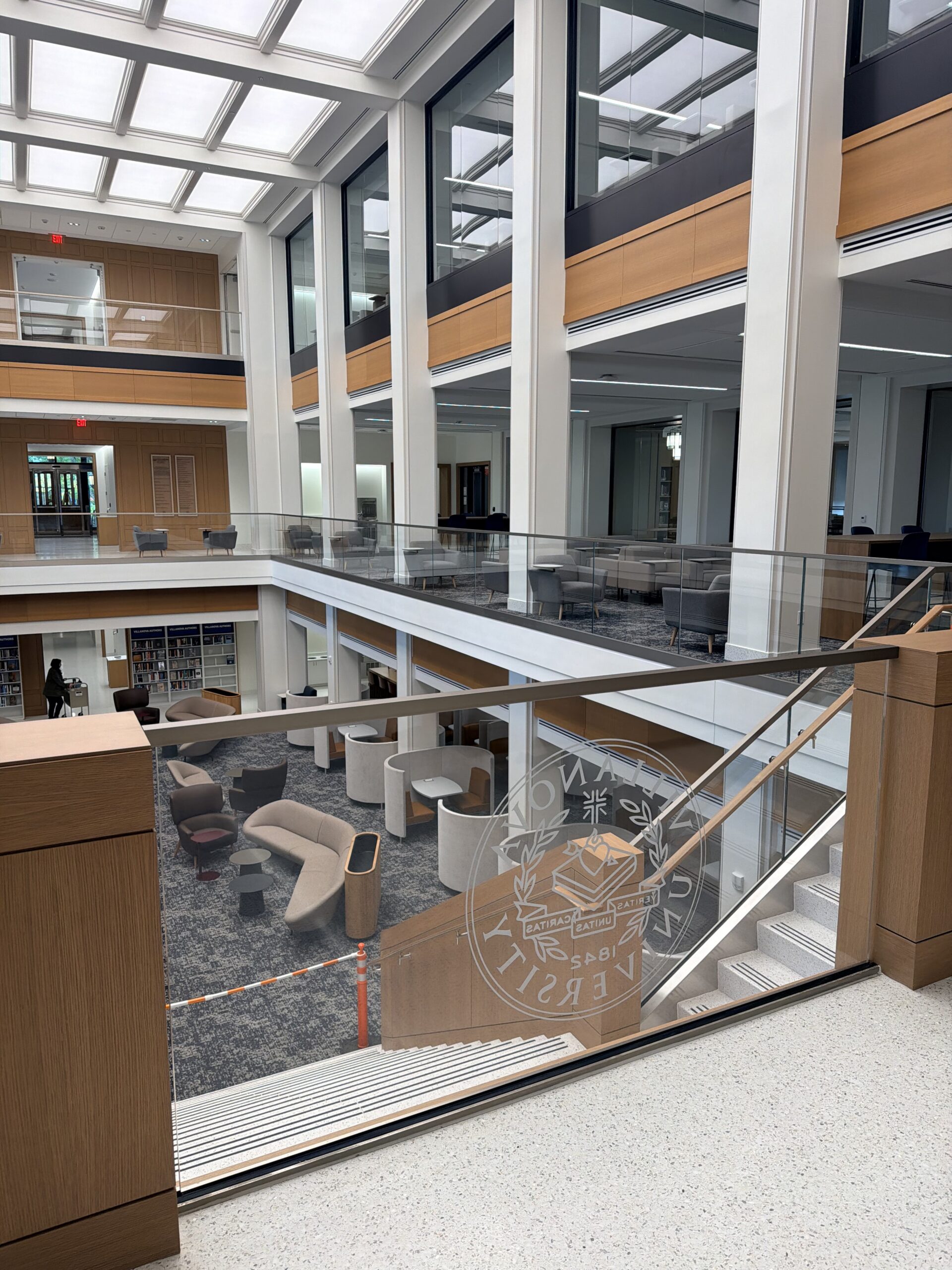 Frameless glass guardrail with the Villanova University seal overlooking the New Student Library atrium