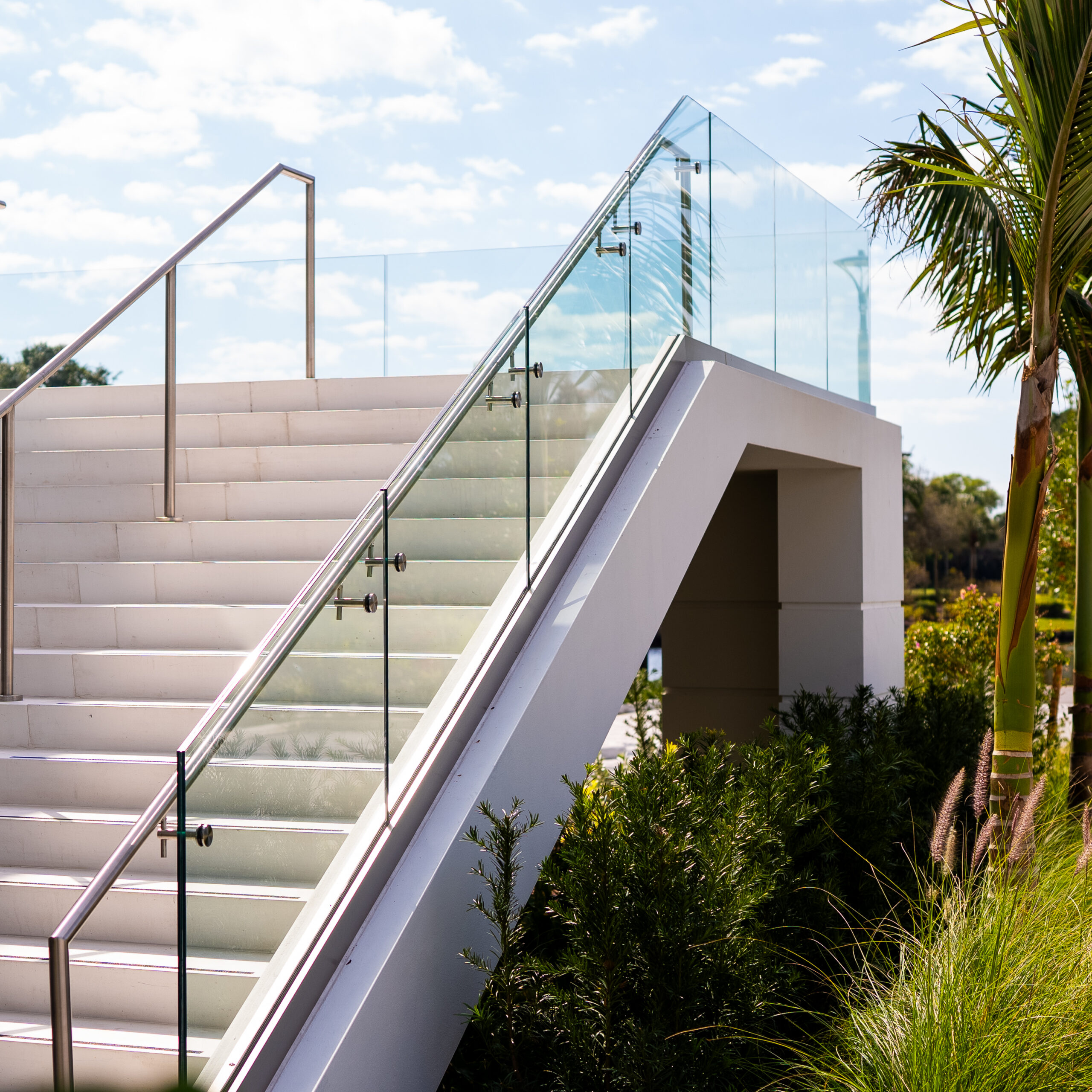 Exterior stair with Brisk M10 base-shoe glass railing framed by palms and landscaping